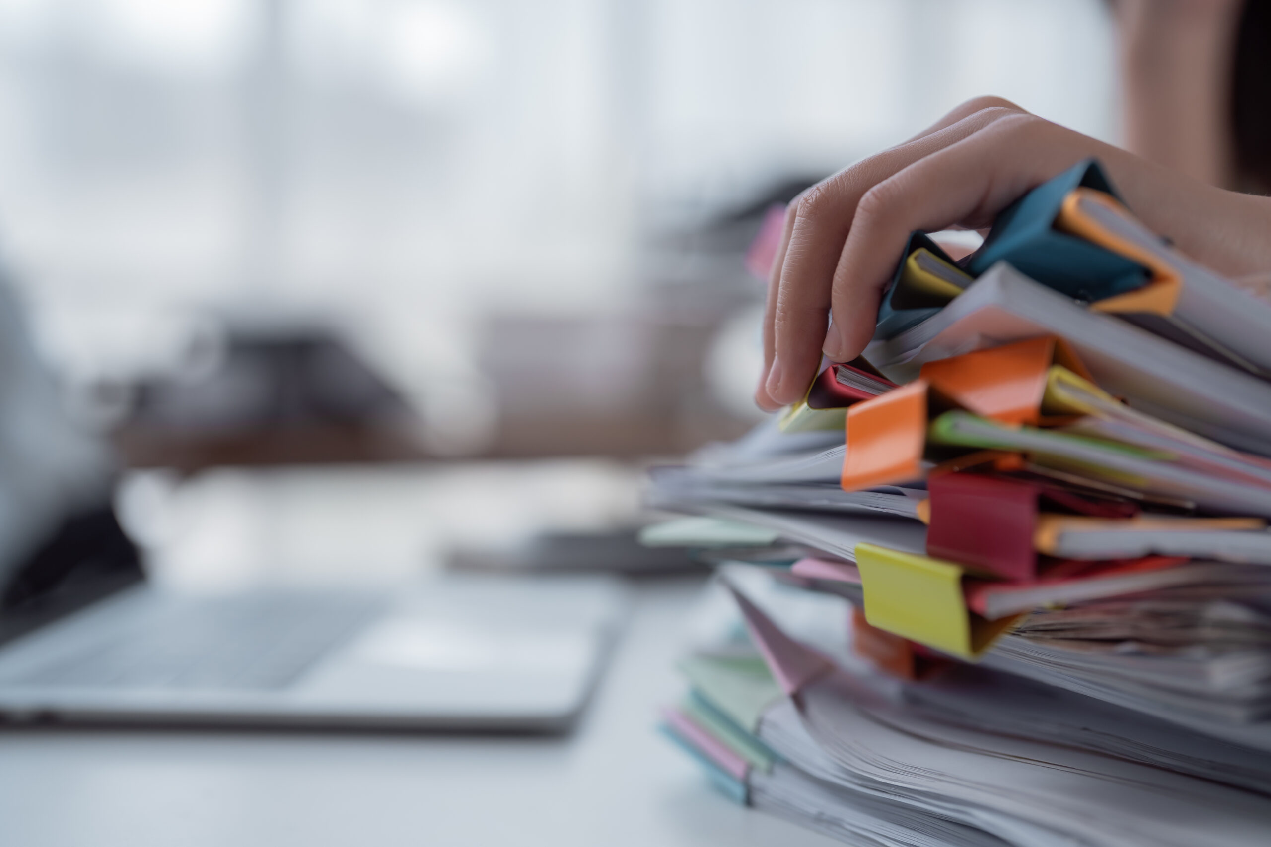 Hand resting on a stack of printed documents organized with colorful binder clips.